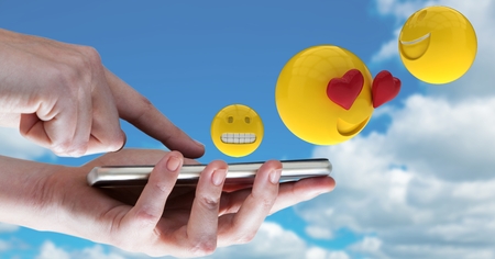 Digital composite of Digitally generated image of emojis flying over hands using smart phone against skyの写真素材
