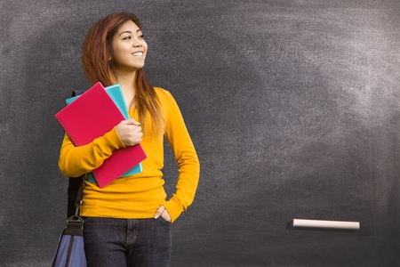 Digital composite of Female student holding books against blackboardの写真素材