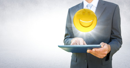 Digital composite of Business man mid section with tablet and emoji with flare against white wallの写真素材