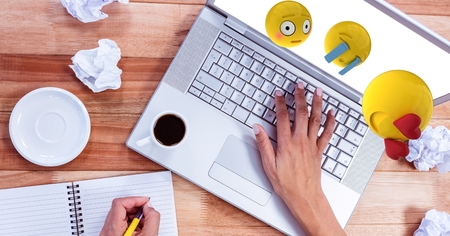 Digital composite of Emojis flying over hands writing in book while using laptopの写真素材