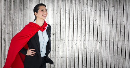 Digital composite of Business woman superhero with hands on hips against grey wood panelの写真素材