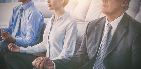 Business people practicing yoga while sitting in living room at officeの写真素材