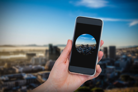 Hand holding mobile phone against white background against cityの写真素材