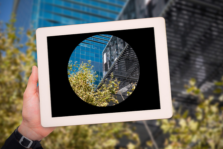 Masculine hand holding tablet against low angle view of modern buildings