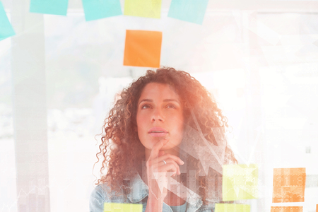 Stocks and shares against thoughtful pretty designer looking at sticky notes on glass window