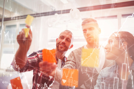 Stocks and shares against colleagues sticking adhesive notes on glass in office