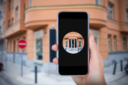 Hand holding mobile phone against white background against entrance of cafe