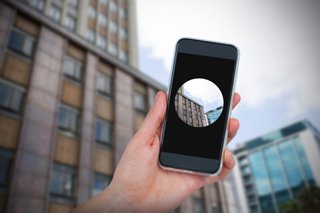 Hand holding mobile phone against white background against view of glass office building