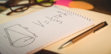 Diagram and equation against black background against high angle view of notepad and pen on deskの写真素材