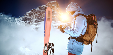 Skier with skis and backpack using mobile phone against view of snowy mountain range and cloudsの写真素材