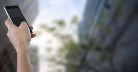 Digital composite of Hand with phone against blurry buildings and skyの写真素材