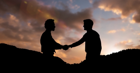 Digital composite of Silhouette business partners shaking hands on mountains during sunsetの写真素材