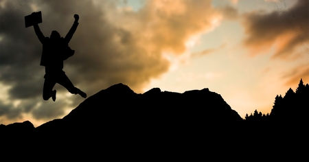 Digital composite of Silhouette businessman jumping on mountain during sunsetの写真素材