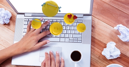 Digital composite of Digital composite image of emojis flying over hand using laptop at tableの写真素材