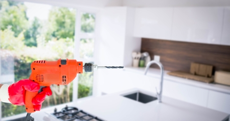 Digital composite of Hand holding drill machine in kitchen