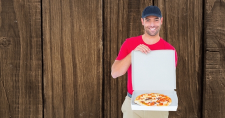 Digital composite of Smiling delivery man showing pizza against wooden wallの写真素材