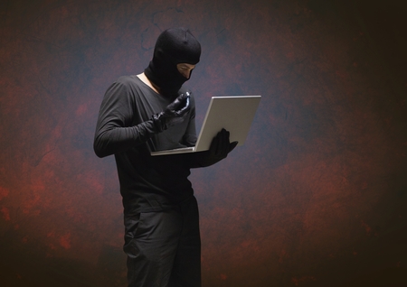 Digital composite of Criminal with laptop against dark background