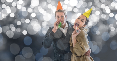 Digital composite of Happy couple blowing party horns against blur background