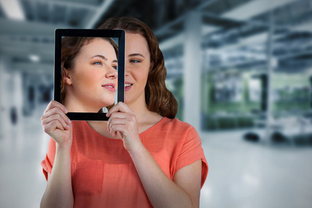 Beautiful woman holding digital tablet in front of her face against classroomの写真素材