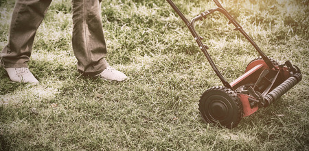 Low section of a man with lawnmower on grassy field in yardの写真素材