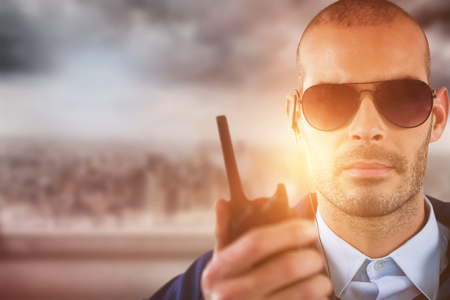 Portrait of security officer talking on walkie talkie against cityscapeの写真素材