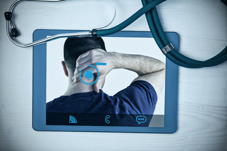 Rear view of a man with neck pain against tablet and stethoscope on deskの写真素材