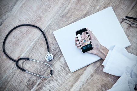 Woman with back injury against doctor using smartphone on wooden deskの写真素材