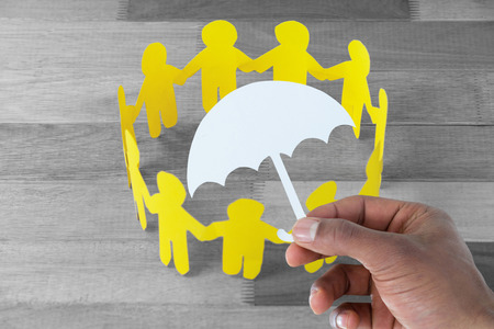 hand holding an umbrella in paper against yellow paper cut out figures formimg circle on wooden...