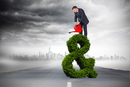 Mature businessman using watering can against open roadの写真素材