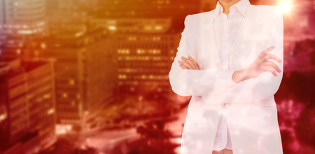 Mid section of businesswoman with arms crossed against illuminated roads by buildings in cityの写真素材