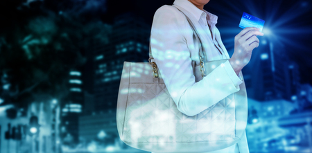 Mid section of woman holding credit card against illuminated roads by building in cityの写真素材