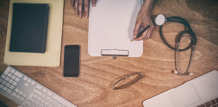Overhead view of doctor writing on clipboard at desk in hospitalの写真素材