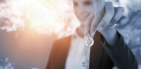 Smiling businesswoman showing new house key against view of beautiful sky and cloudsの写真素材