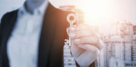 Mid section of businesswoman showing new house key against modern skyscrapers in cityの写真素材