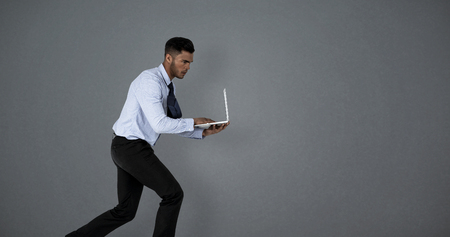 Businessman using laptop while running  against grey backgroundの写真素材