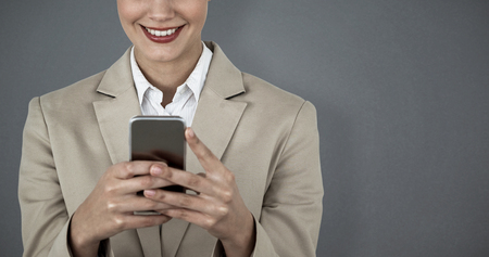 Close up of smiling businesswoman using mobile phone against grey backgroundの写真素材