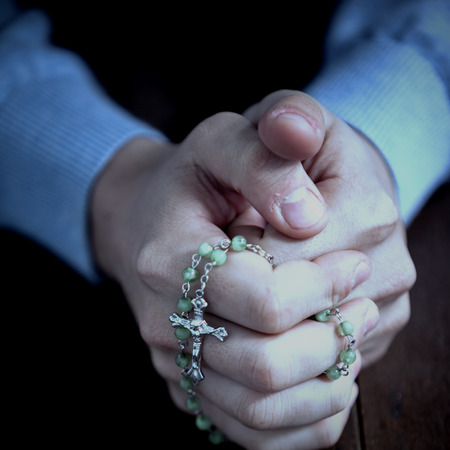 Praying hands of man with rosary on wooden deskの写真素材