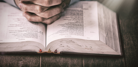 Mid section of man praying with bible at wooden desk