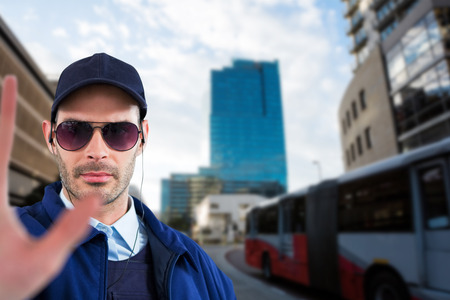 Confident security officer showing stop gesture against cityscape against cloudy skyの写真素材