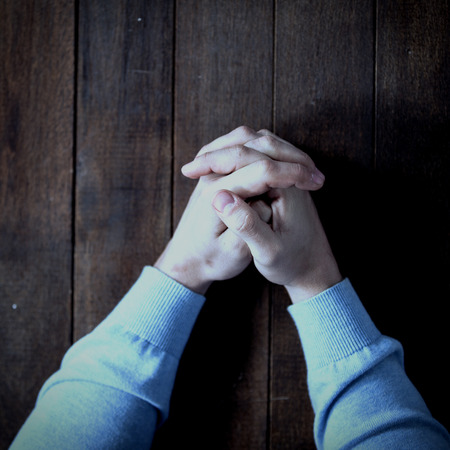 Cropped image of man praying on wooden tableの写真素材