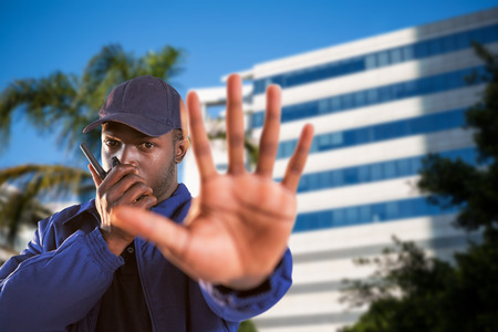 Portrait of confident security talking on walkie talkie and making stop gesture against tree by...
