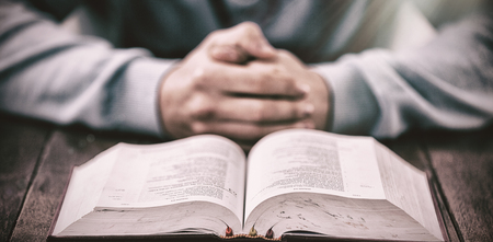 High angle view of man with bible praying at wooden tableの写真素材