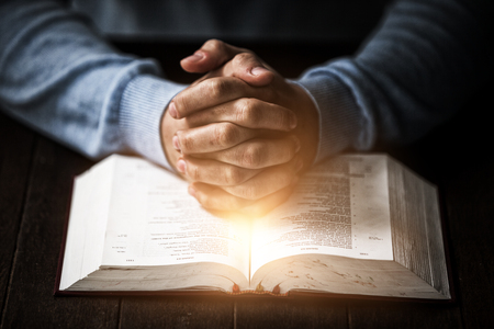 Bright spot of a flare against mid section of man praying with bibleの写真素材