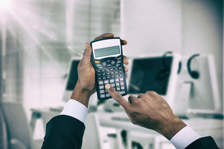 Cropped hands of businessman using calculator  against computers and headsets