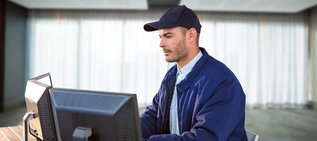 Serious security officer using computer against spacious room with curtains on window