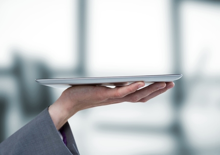 Digital composite of Hand with tablet against blurry grey officeの写真素材