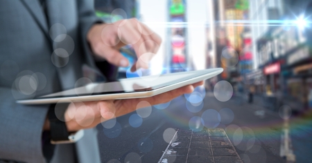 Digital composite of Business man mid section with tablet behind bokeh against blurry street