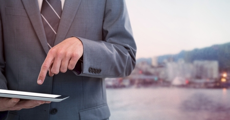 Digital composite of Business man mid section with tablet against blurry skyline and red overlayの写真素材