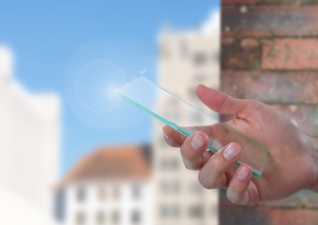 Digital composite of Hand holding glass screen with brick wall and buildingsの写真素材