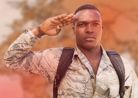 Digital composite of Soldier with backpack saluting against blurry brown map and red overlay